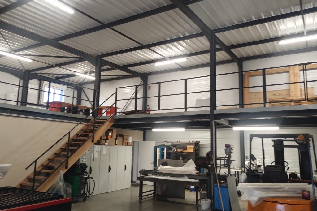 Intérieur d'un atelier avec un mezzanine, des escaliers en bois et des équipements de fabrication.